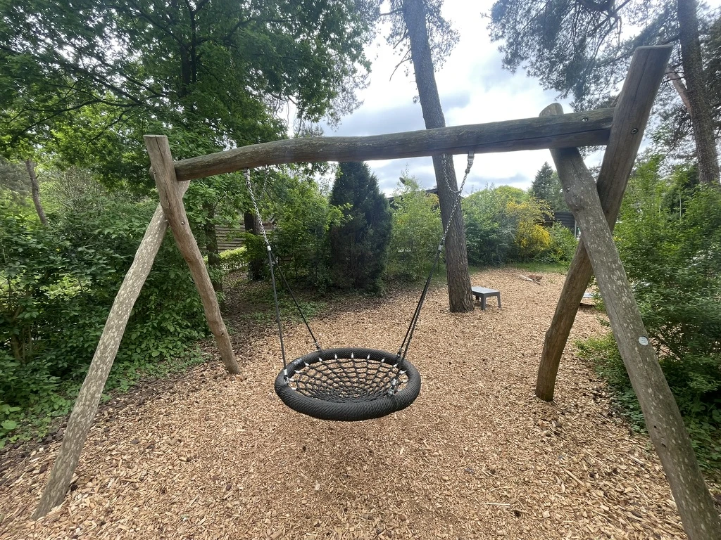 Een ronde nestschommel tussen de bomen in de speeltuin